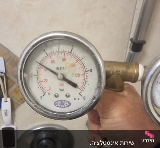 מד לחץ מים ביד של אדם ליד ברז